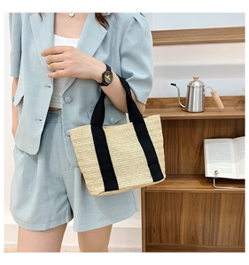 Detail of beige straw handbag with black handles and V-shaped weave in lifestyle setting