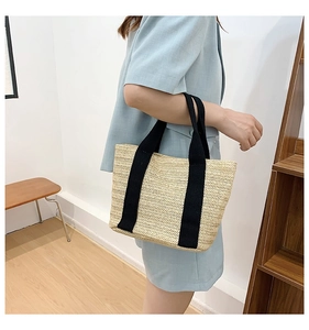 Detail of hand-woven straw tote bag with black canvas straps in a casual lifestyle setting