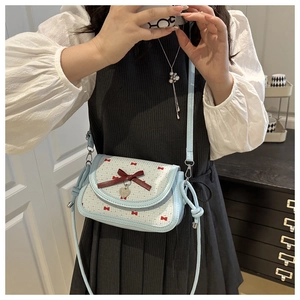Detail of light blue crossbody bag with red bow print and silver heart pendant