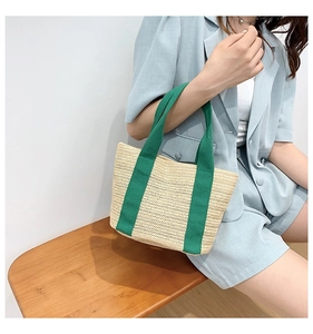 Detailed close-up of straw woven tote bag featuring green canvas handles and texture
