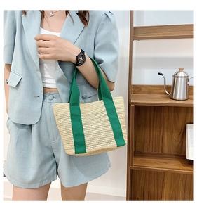 Detail of woven straw tote bag with green fabric handles held by a model in blue suit