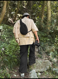 Close-up of black crossbody chest bag with round metal zipper and beige utility shirt