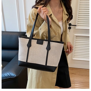 Detail of color-block tote bag featuring cream canvas and black leather strap textures