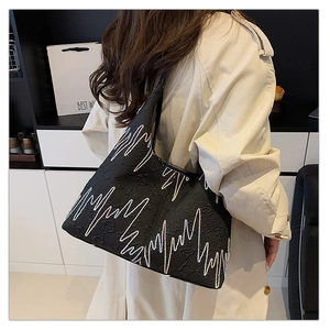 Detail of black underarm tote bag with monogram embossing and colorful wave embroidery