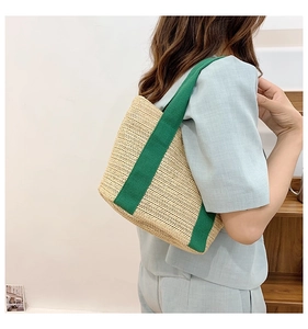 Side view of a woven straw tote bag with contrasting dark green canvas handles on a model