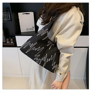 Detail of black tote bag with pulse embroidery shown on a model in a beige trench coat