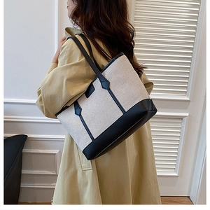 Detail of minimalist canvas and black leather tote bag worn with a classic trench coat