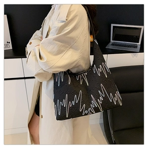 Detail of a black textured tote bag with wave patterns worn with a beige trench coat