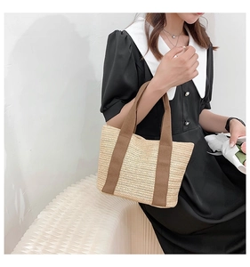 Detail view of handmade straw tote bag with brown fabric handles held by a model