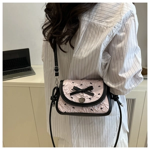 Detail of pink pleated crossbody bag with black bows and heart charm on a desk