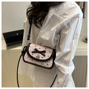 Close-up of pink embossed fabric texture with black bow and heart pendant on shoulder bag