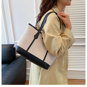 Minimalist canvas tote bag with black leather trim shown on shoulder in a modern setting