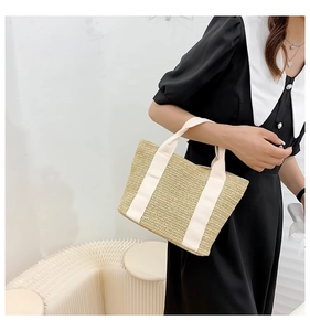 Detail of woven straw handbag with white canvas straps on minimalist paper stool
