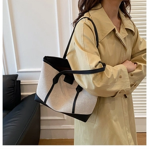 Détail d'un grand sac cabas en toile et cuir porté avec un trench dans un intérieur