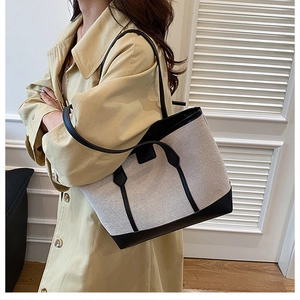 Side view of model carrying a minimalist beige woven canvas and black leather tote bag