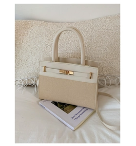 Detail of minimalist bi-color handbag with woven texture and gold clasp on a cozy bed