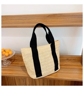 Detailed close-up of handmade straw woven bag with black canvas straps on wooden shelf