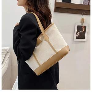 Detail of canvas tote bag with brown leather trim shown on shoulder in a cozy interior