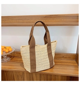 Detail of woven straw bag with beige herringbone texture and brown canvas handles