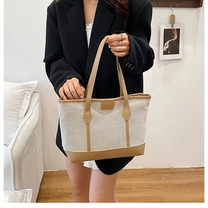 Detailed view of canvas tote bag with khaki leather trim held by professional model