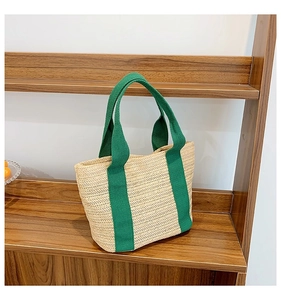 Detail of hand-woven straw tote bag featuring green fabric handles and chevron pattern