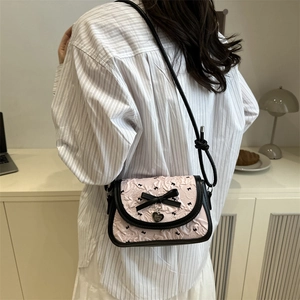 Pink crossbody bag with black ribbon bow and heart charm shown on a female model