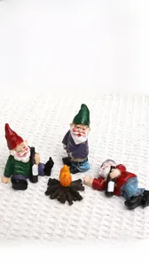 Close-up of funny resin Christmas gnomes sitting around a campfire on a plaid surface