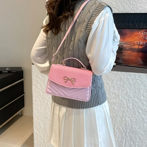 Pink crossbody bag with woven texture and gold bow detail shown on a model