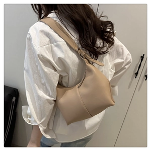 Detail of minimalist beige leather hobo bag with adjustable strap on model's shoulder