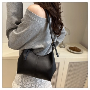 Detail of minimalist black faux leather shoulder bag with vertical seam and adjustable strap
