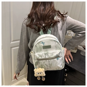 Detail of white mini backpack with green bamboo leaves, blue butterfly and plush charm