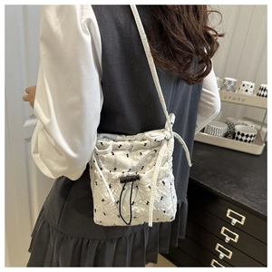 Lifestyle view of a white quilted tote bag with black bow print and adjustable strap