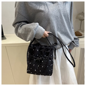 Detail of black quilted bucket bag with white ribbon print and drawstring closure