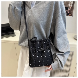 Detail of a black quilted drawstring crossbody bag with white floral rabbit embroidery