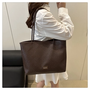 Side view of large coffee brown woven tote bag on shoulder against minimalist interior