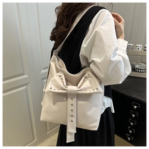 Model wearing a cream leather tote bag with a large studded bow detail and silver rivets
