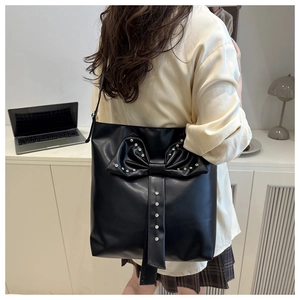 Lifestyle shot of a black tote bag featuring a sparkling rhinestone bow on a shoulder strap