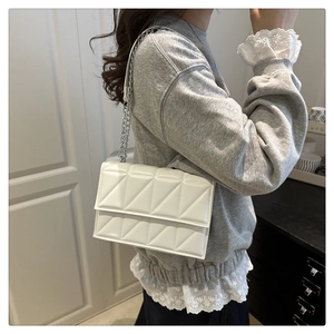 Close-up of a white quilted shoulder bag with silver chain strap shown on a model