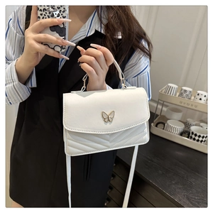 Detailed shot of white quilted shoulder bag with gold butterfly clasp and top handle