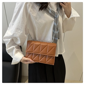 Detail view of caramel brown quilted shoulder bag with silver chain strap on a model