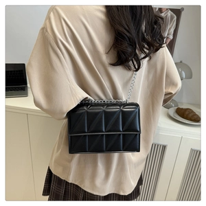 Rear view of a black quilted crossbody bag with silver chain strap worn by a woman
