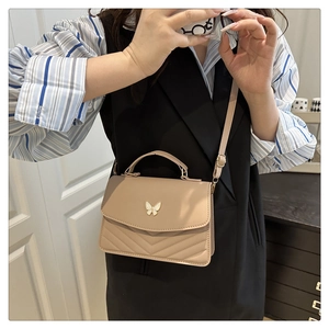 Detail of beige small crossbody bag featuring a butterfly buckle and V-shaped stitching