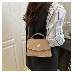 Detail of a beige quilted crossbody bag with golden butterfly clasp and top handle