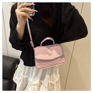 Detail of pink crossbody bag featuring V-shaped quilting and a metal butterfly clasp