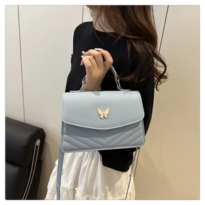 Detail of light blue crossbody bag with gold butterfly clasp and V-quilted pattern