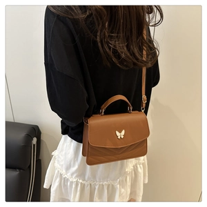 Detailed view of the brown leather handbag featuring a white butterfly ornament and V-stitching
