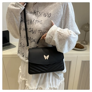 Detail of black quilted shoulder bag with gold butterfly clasp shown on model