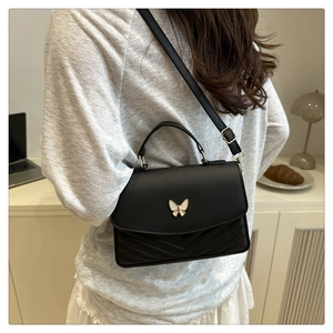 Model wearing a black quilted crossbody bag with metal butterfly buckle in a cozy room