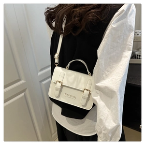 Close-up of white leather crossbody bag showing gold metal buckles and adjustable strap