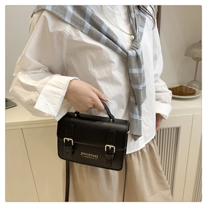 Detail of a chic black PU leather handbag with metal buckles held by a model in casual wear
